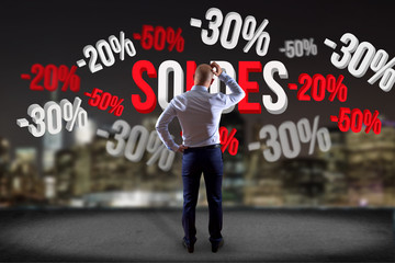 Businessman in front of a wall with sales promotion 20% 30% and 50% flying on an interface - Shopping concept