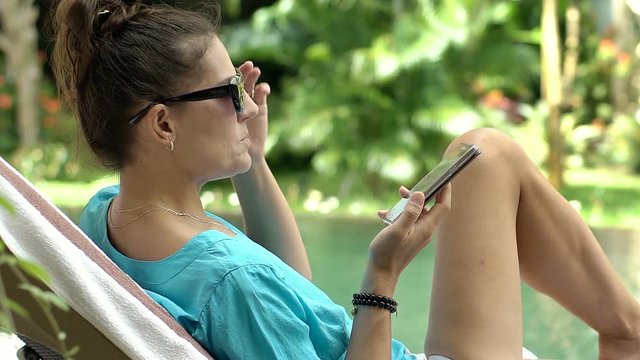 Woman talking on loudspeaker while relaxing on sunbed and eating fruits, steadycam shot
