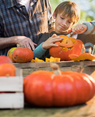 Fototapeta premium Father teaching his son how to carve a pumpkin for halloween.