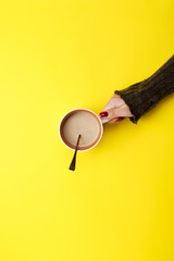Girl holding a mug of coffee on a yellow background. The concept of a pause, a break.