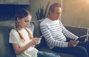 Ignoring father and daughter sitting on sofa with gadgets