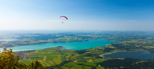 Paraglider flies over the green valley with lakes and towns. Area of the city of Fussen, Germany