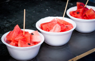 Fresh watermelon slice in white foam plate container on black wooden table