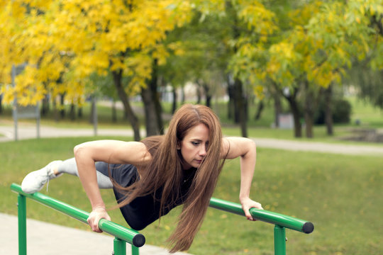 Beautiful female athlete exercising on parallel bars, doing push-ups