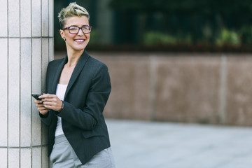 Portrait of happy business woman standing on street. She smiling and talking on her cell phone.