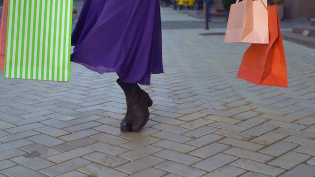 close-up of feet. a happy girl in autumn winter boots sants with happiness. the girl has a bright, long, fiolet dress. a lot of bright paper bags can be seen in the frame. the woman is dancing on the