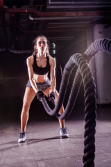Fototapeta na wymiar Battle ropes session. Attractive young fit and toned sportswoman working out in fitness training gym