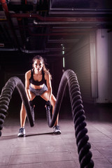 Battle ropes session. Attractive young fit and toned sportswoman working out in fitness  training gym