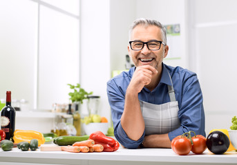 Smiling man posing in the kitchen, he is preparing healthy homemade food using fresh organic...