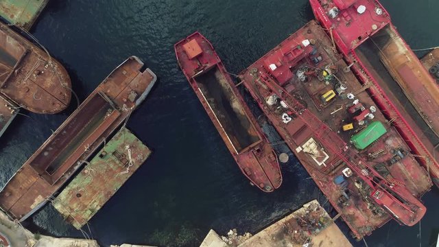 Ascending aerial bird eye view of an abandoned shipyard with docked decommissioned old broken ships and boats