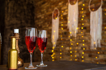 Two glass glasses, a decanter with pink champagne, wine, stand on a blurry background of a brick wall, candles, a herring in the background, bokeh. Romantic evening, date. Place for the inscription.