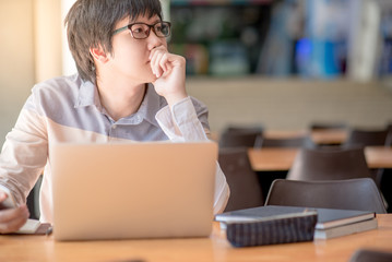 Young Asian business man feeling stressed, tired and headache during working with laptop computer in public co working space. freelance lifestyle in workspace.