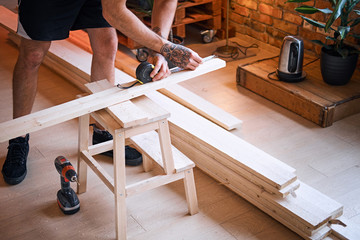 Carpenter drilling a hole in a board in a room with loft interior.
