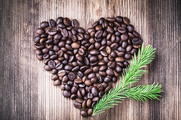 Coffee beans in the shape of heart with fir tree branch on wooden background