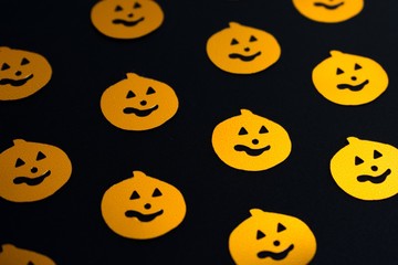 Shiny seamless pattern created from halloween party confetti, orange pumpkins on black non reflective background