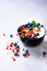 Tasty homemade granola, yogurt, fresh organic berries, pomegranate, mint on grey concrete background with copy space, top view.