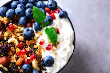 Tasty homemade granola, yogurt, fresh organic berries, pomegranate, mint on grey concrete background with copy space, top view.