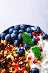 Tasty homemade granola, yogurt, fresh organic berries, pomegranate, mint on grey concrete background with copy space, top view.