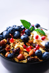 Tasty homemade granola, yogurt, fresh organic berries, pomegranate, mint on grey concrete background with copy space, top view.