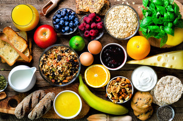 Healthy breakfast ingredients, food frame. Granola, egg, nuts, fruits, berries, toast, milk, yogurt, orange juice, cheese, banana, apple on wooden rustic background, top view, copy space