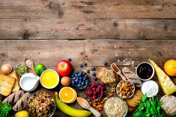 Healthy breakfast ingredients, food frame. Granola, egg, nuts, fruits, berries, toast, milk, yogurt, orange juice, cheese, banana, apple on wooden rustic background, top view, copy space