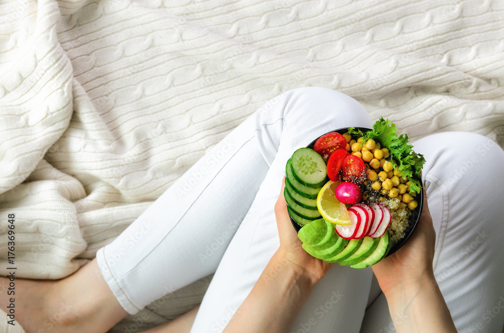 Wall mural girl in white jeans holds in hands fork, vegan breakfast meal in bowl with avocado, quinoa, cucumber