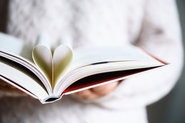 Book with opened pages and shape of heart in girl hands. Copy space. Love concept