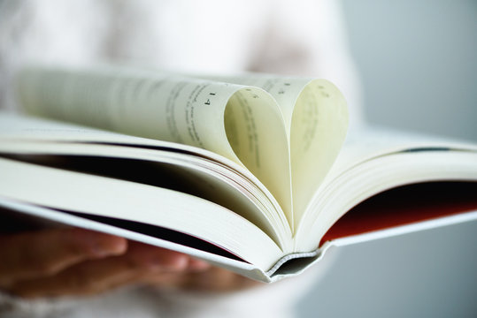 Book with opened pages and shape of heart in girl hands. Copy space. Love concept