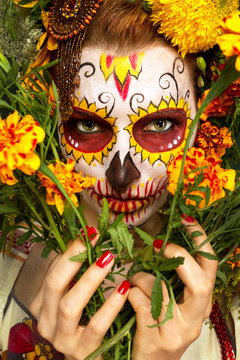 Женщина с разрисованным лицом к мексиканскому Дню Мертвых с цветами.