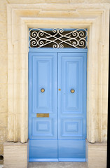 Light blue wooden entrance door with ornated sign and knocker 