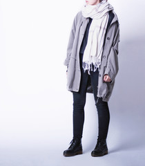 Woman wearing casual outfit with oversized parka jacket, black skinny jeans, big white scarf and black laced faux leather biker boots on white background. Copy space. Autumn or winter fashion 2017.