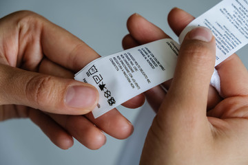 Woman checking the care label. selective focus. Woman's hands holding clothes label with cleaning instructions. lose-up Of Person Reading The Clothing Label Showing Washing Instructions.