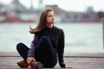 Young adult woman sitting on a wooden jetty on the river