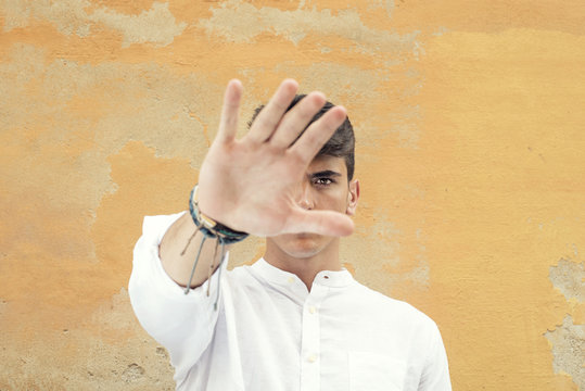 Retrato en primer plano de hombre joven con camisa blanca. Expresi&oacute;n seria y mano tapando el objetivo de la c&aacute;mara. Solo se le ve un ojo.
