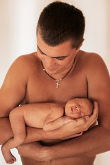 Naklejka premium Naked father holds tiny newborn baby on his arms