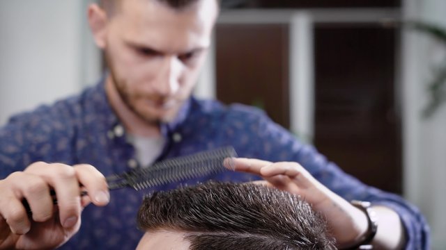 close up shot of the head of a man who combs his hair and makes a fashionable styling in barbershop with a comb and a hair gel