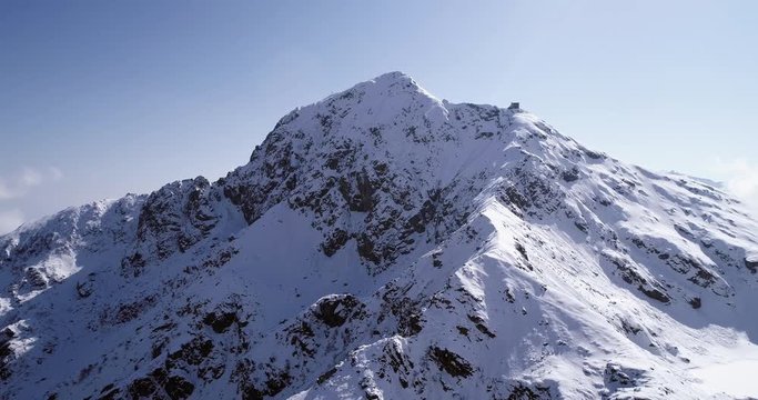 aerial flying moving backward over snowy mountain peak ridge establisher. Outdoor snow alpine wild nature scape in winter. 4k drone flight establishing shot