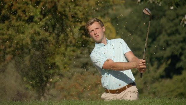 A Celebrating Golfer chips out of a sand trap and drops the ball into the cup in slow motion.