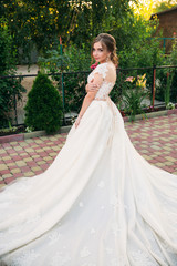 Fototapeta premium Young girl in wedding dress in park posing for photographer. Sunny weather, summer.