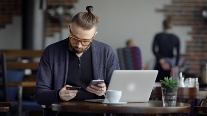 Young man making Internet purchase. Young male in glasses sitting with laptop at cafe and making Internet purchase.