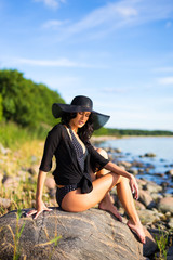 beautiful woman in bikini sitting on big stone on rocky beach
