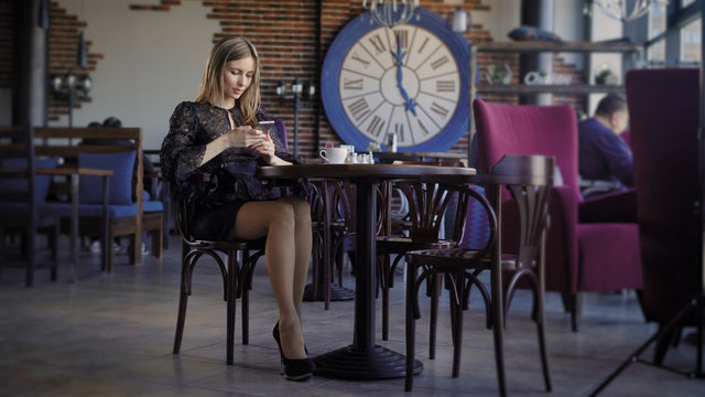 young cute woman using phone ,sitting at a cafe holding a smartphone, answering texts. Beautiful business woman in a restaurant during a lunch break, browsing messages online.