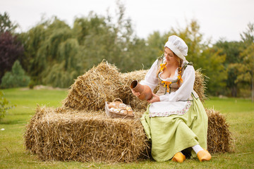 Naklejka na ściany i meble Peasant woman sits on the hay and pours milk