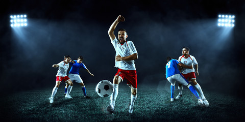 Soccer players performs an action play on a dark background. Soccer players fight for the ball. Players wears unbranded sport uniform. © Alex