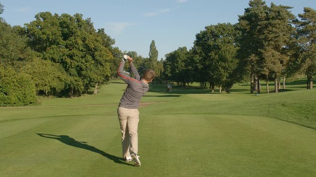 A Golfer drives a shot down a fairway on a golf course.