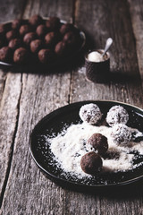 Homemade healthy vegan chocolate balls, truffles, candies sprinkled grated coconut in the plate on the vintage wooden table. Selective focus. Haze effect 