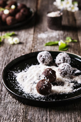 Homemade healthy vegan chocolate balls, truffles, candies sprinkled grated coconut in the plate on the vintage wooden table. Selective focus 