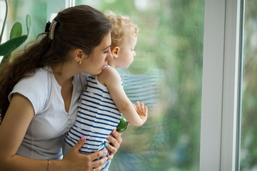 Young mother and son watching the rain through the window