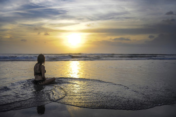 free woman sitting looking to sea sunset practicing yoga and meditation at beautiful Asian beach