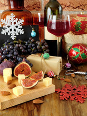 Cheese and figs on a wooden board, red wine in a glass, grape and Christmas attributes around. Christmas table laying
